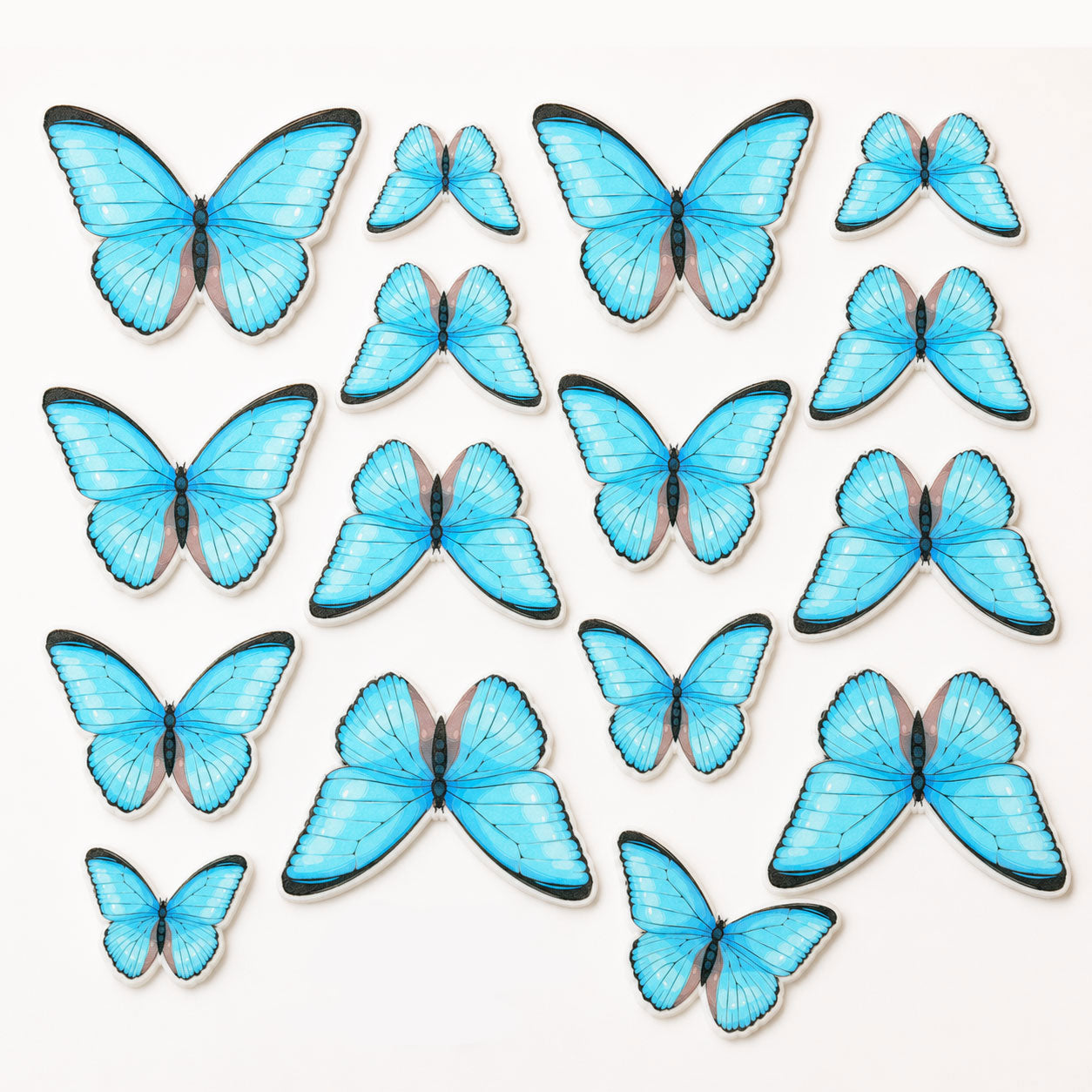 Flat lay of 16 precut edible blue butterfly cake toppers arranged on a white background