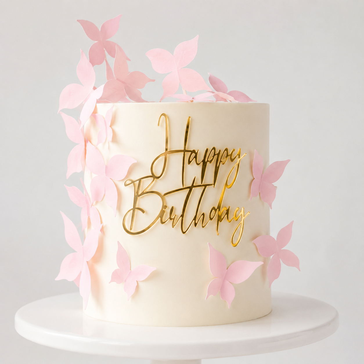 Single-tier cream cake with pink wafer paper butterflies cascading down one side and a gold mirror acrylic Happy Birthday topper