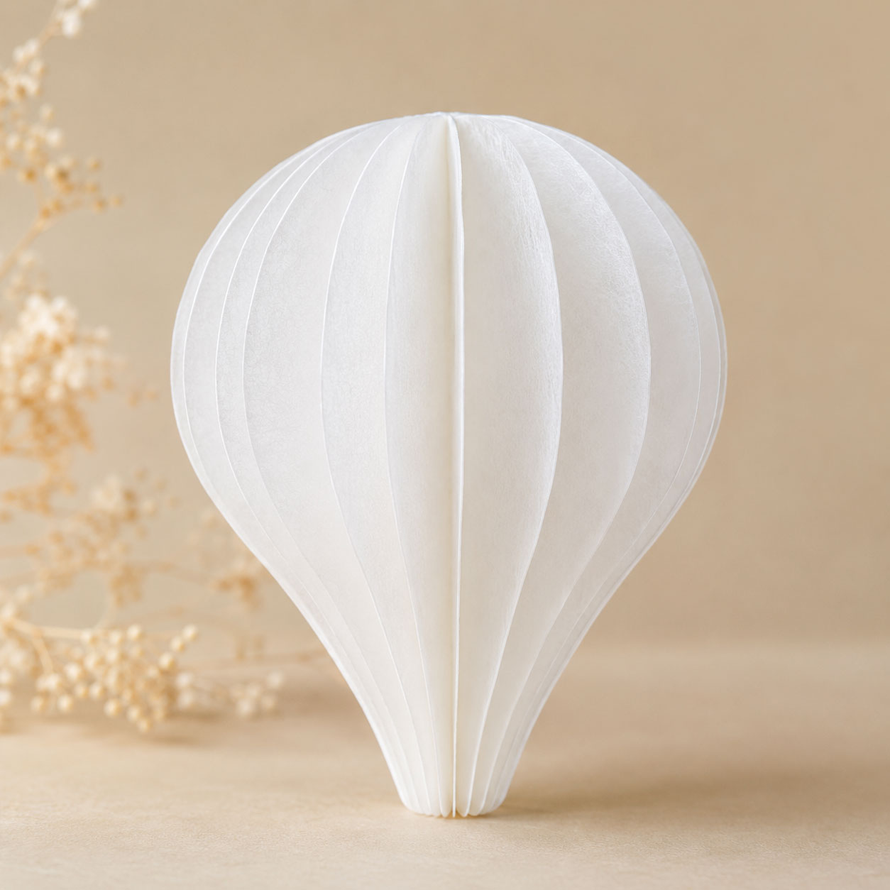 Single dimensional balloon-shaped decoration assembled from layered white wafer paper segments on a beige background