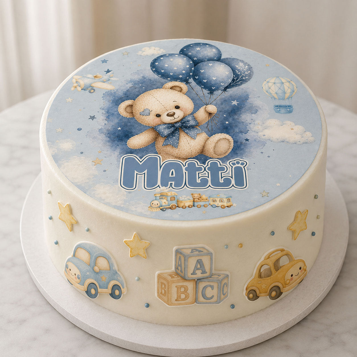 Baby boy teddy bear edible cake topper set displayed on a round frosted birthday cake