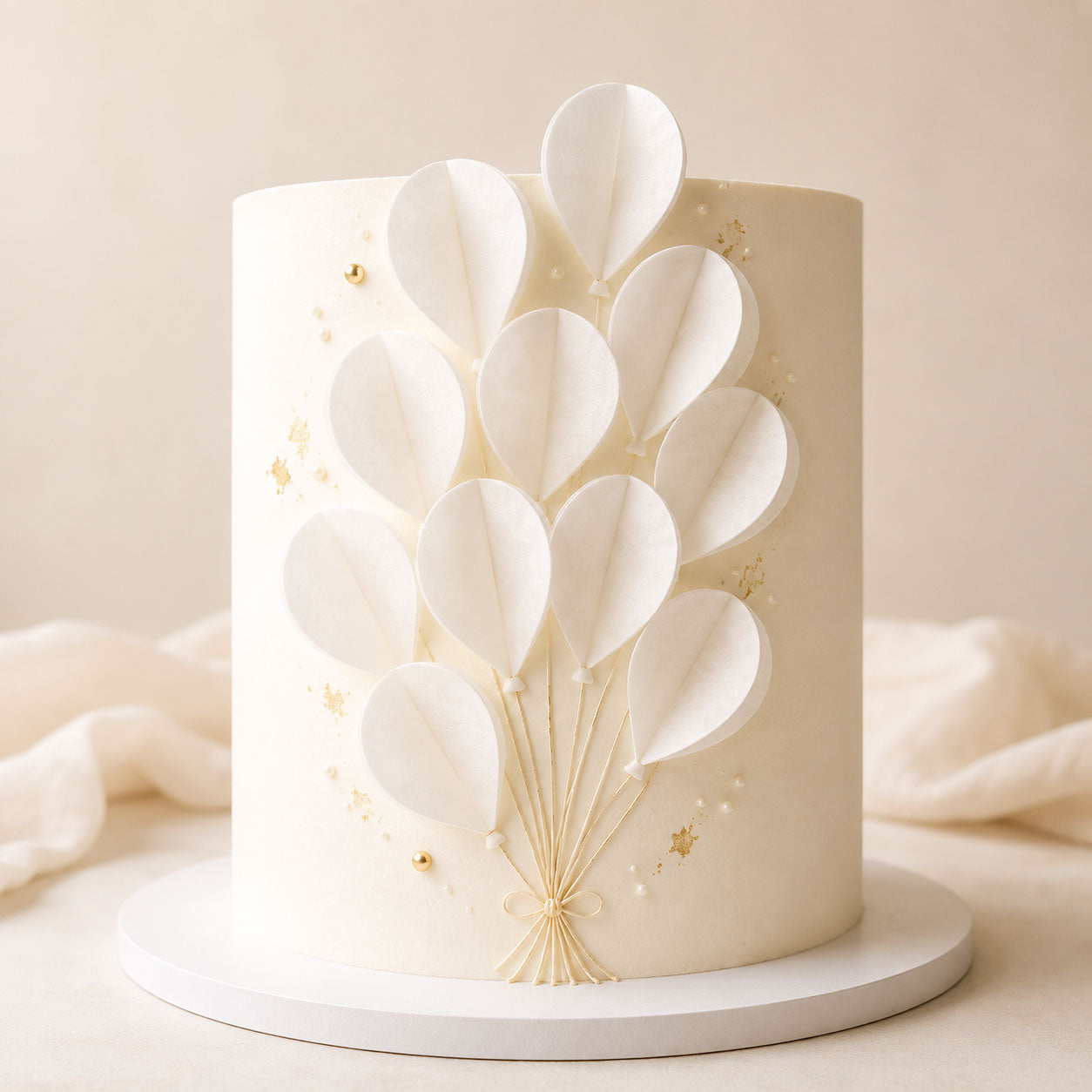 Ivory cake decorated with a bouquet of white wafer paper balloon-shaped segments tied with a gold string bow and gold pearl accents