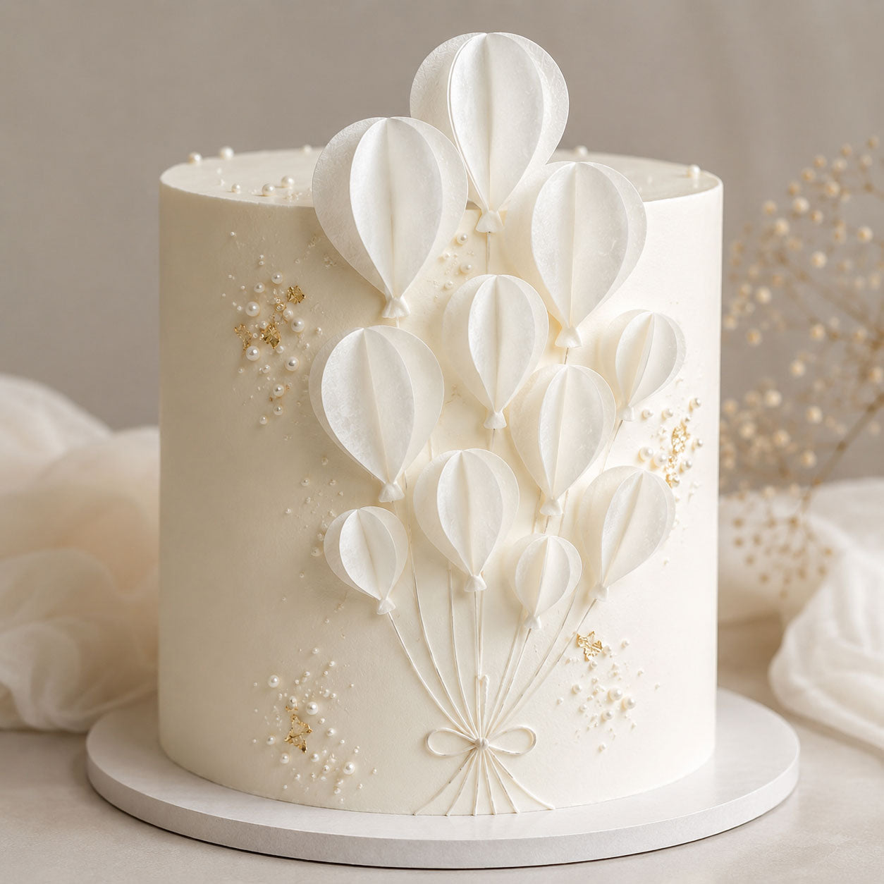 Ivory cake with pearl and gold-leaf accents decorated with a bouquet of assembled white wafer paper balloon segments